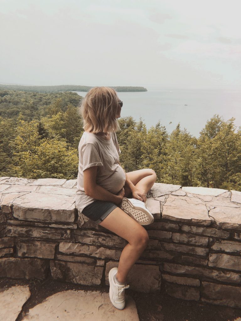 pregnant girl looking at the view from peninsula state park in door county, beige maternity t-shirt, H&M basic oversized tee, everlane tread trainers, maternity shorts, blond blunt cut bob