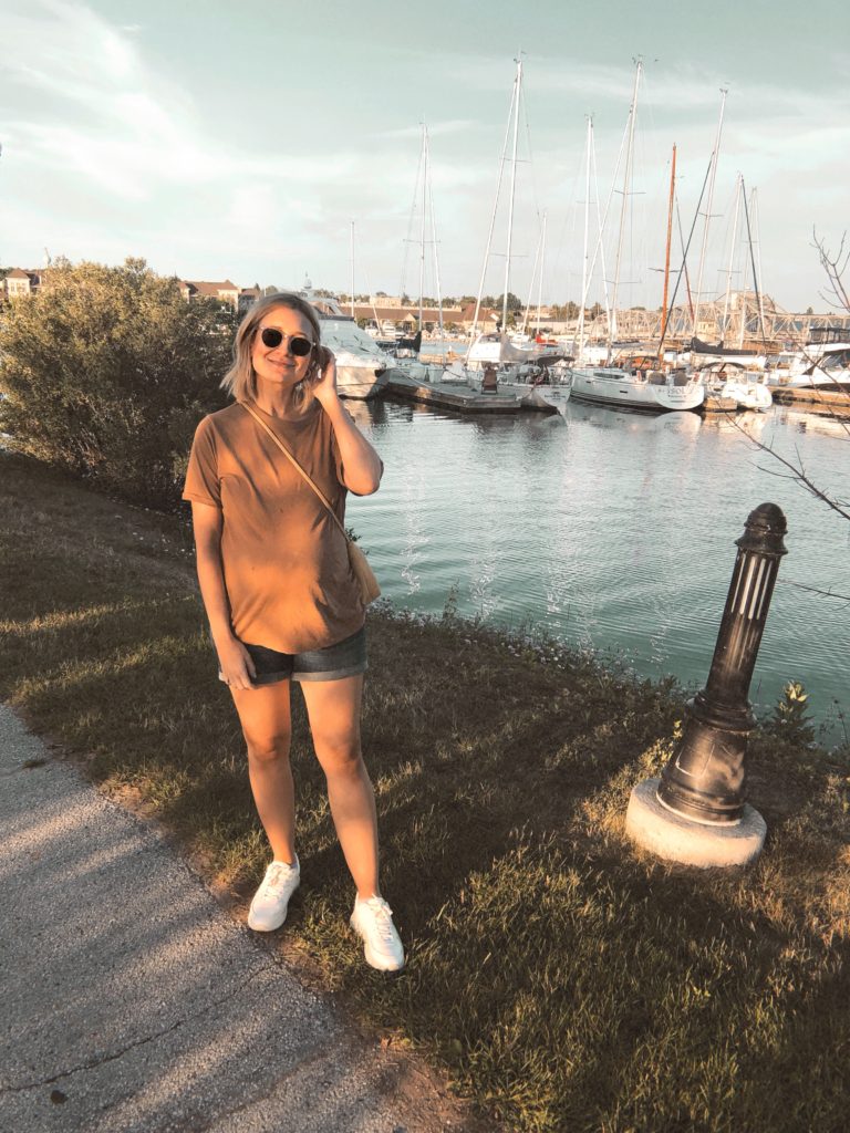 girl standing on a walking path in sturgeon bay wisconsin, view of the sailboats, everlane oversized tee, caramel colored t-shirt, maternity shorts, everlane tread sneakers, blonde shoulder length bob